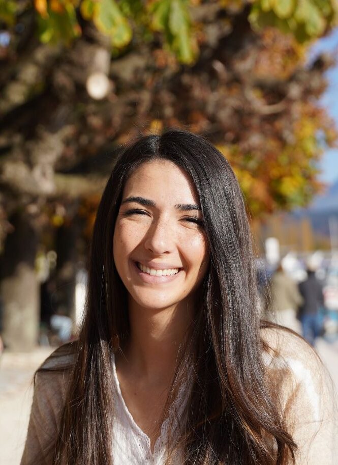 Smiling female Montessori teacher with long brown hair posing for a portrait with fall leaves in background