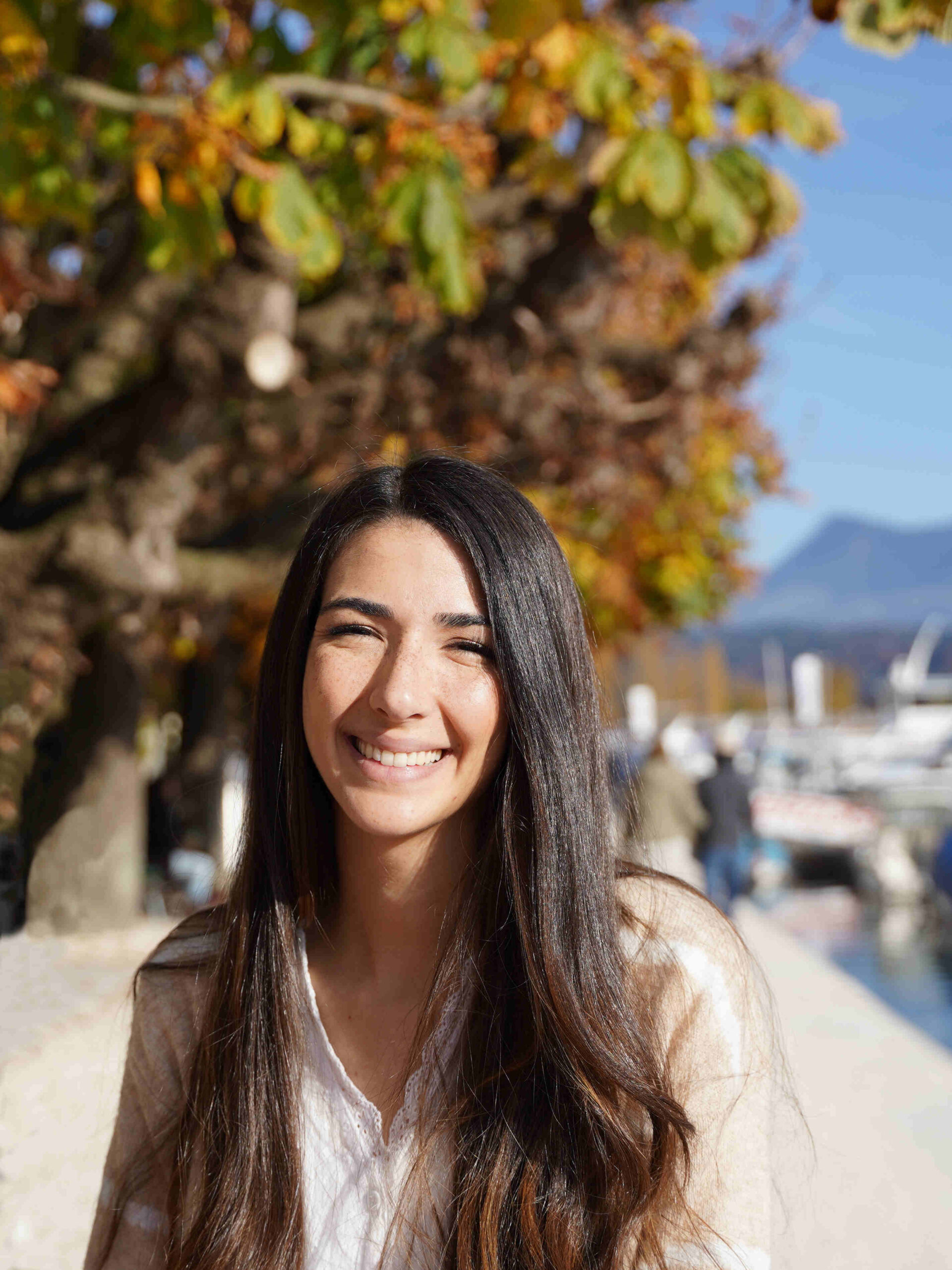 Young woman with brown hair walking by lake Lucerne with fall colored leaves in background