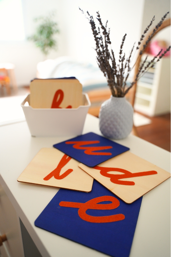 Montessori sand paper letters spread out on a desk next to a white vase of dried lavender.