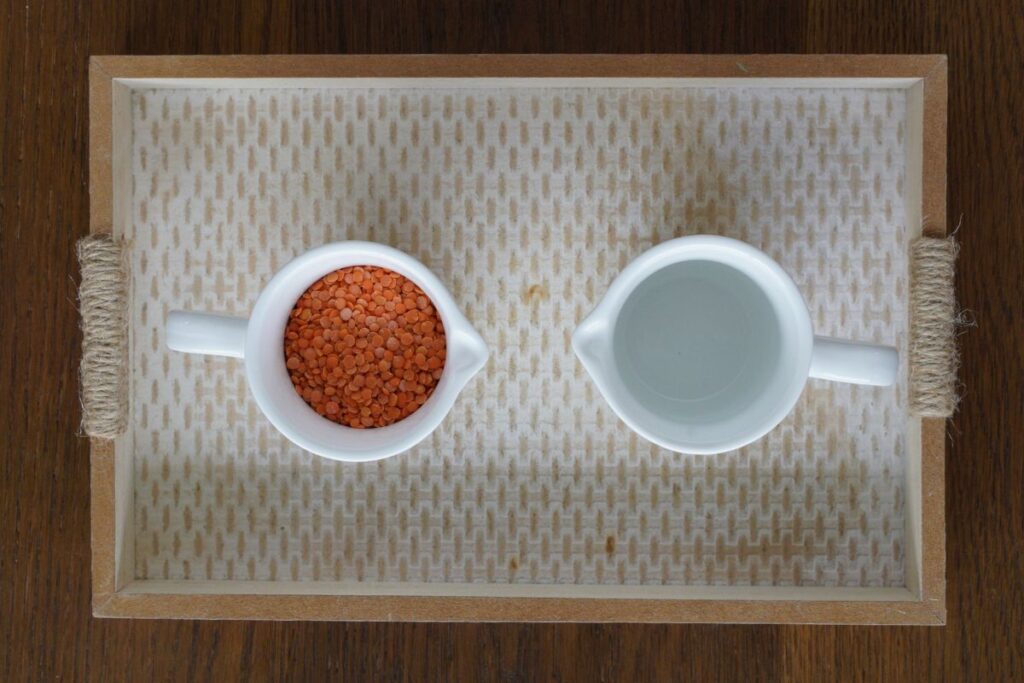 Montessori Practical Life dry pouring activity with two small pitchers, one filled with red lentils, to help children practice coordination, concentration, and independence.