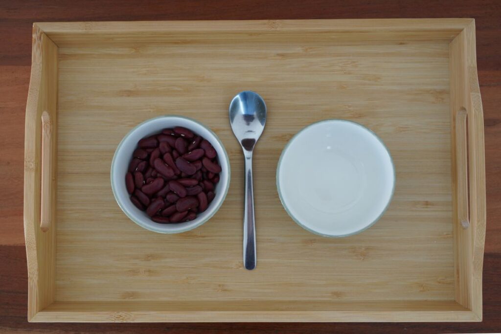 Montessori Practical Life spooning work with two bowls, red beans, and a spoon to help children develop concentration, coordination, and fine motor skills.