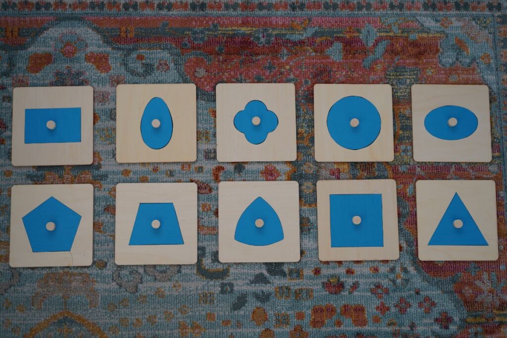 Set of DIY Montessori metal insets with wooden frames and blue geometric shapes used for handwriting preparation and fine motor skill development.