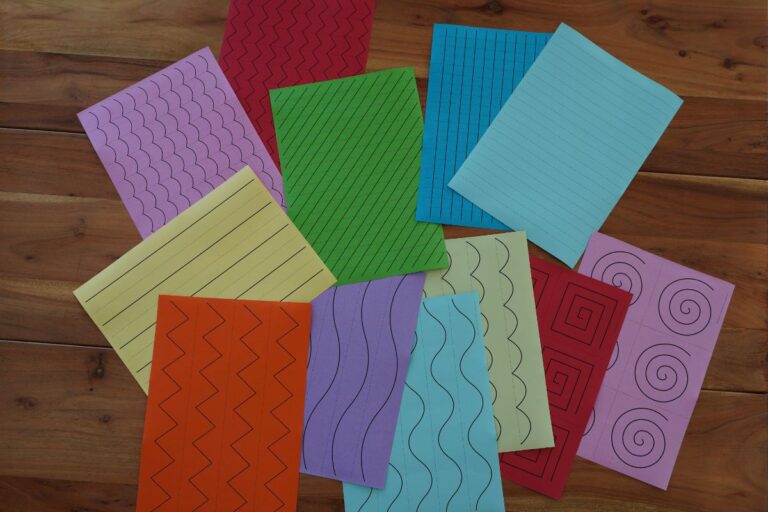 About a dozen sheets of different colored paper with different line papers placed on a wooden table