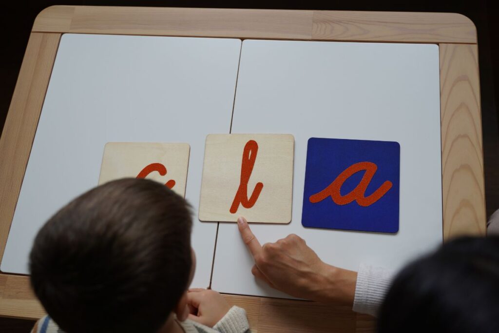 Teacher points to letter 'l' while teaching toddler the montessori sandpaper letters