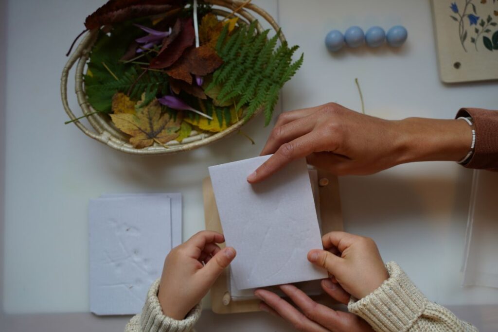 Adult and child placing blotting paper over leaves in a wooden flower press during a Montessori-inspired nature activity.