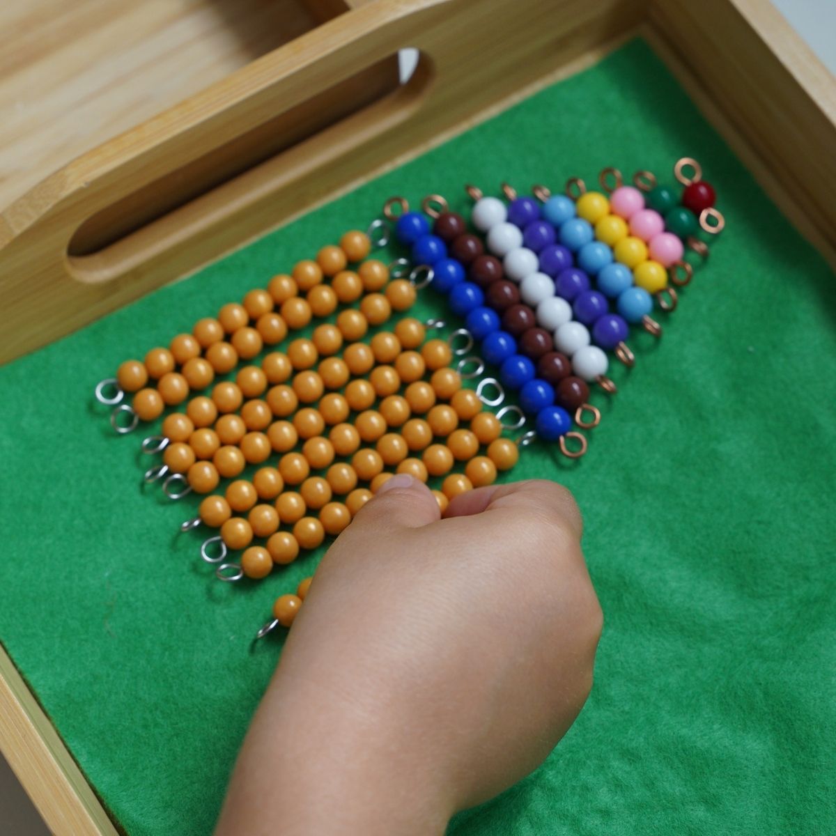 A child uses beads in a tray lined with green felt to complete the Montessori beads activity