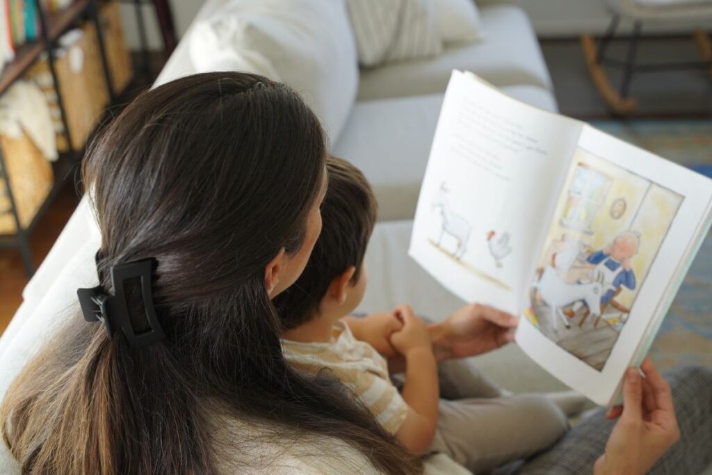 Mother reading a picture book to her young child on the couch, sharing a quiet storytime moment together.