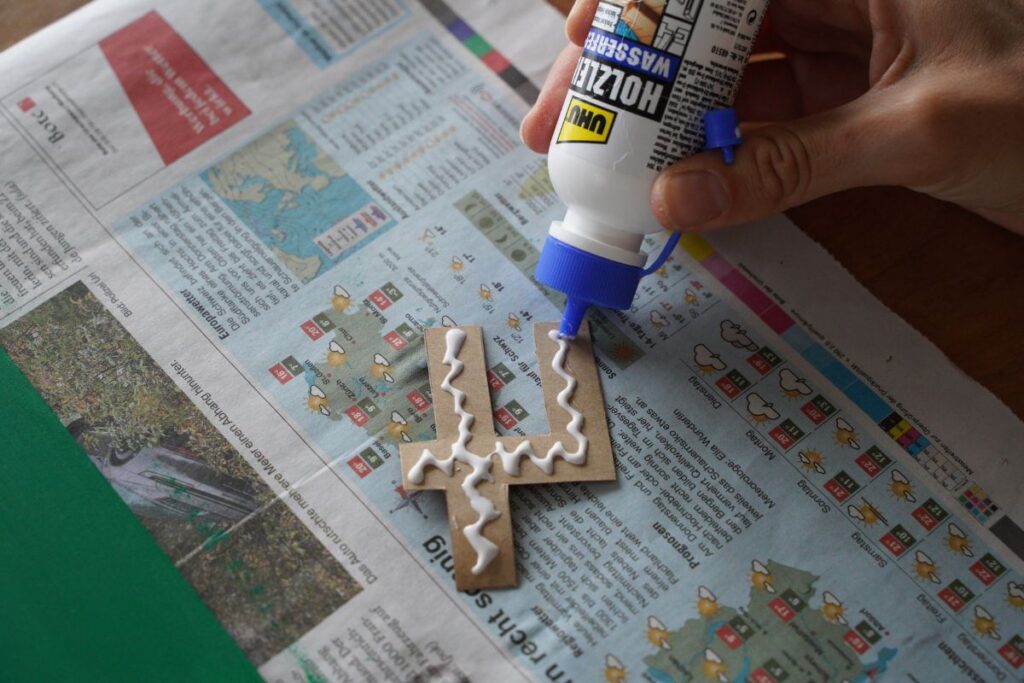 Applying glue to the back of a cut-out number 4 for a DIY Montessori sandpaper numbers activity to create tactile learning materials for children.