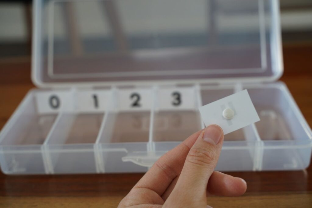 Adult hand holding the back of a Montessori number card, demonstrating how to attach it inside a DIY spindle box for early math activities.