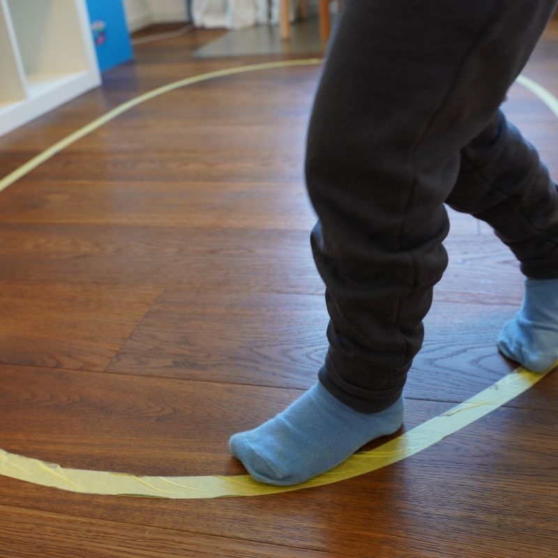 Child walking carefully along a taped line on the floor during a Montessori activity to develop balance, coordination, and concentration.