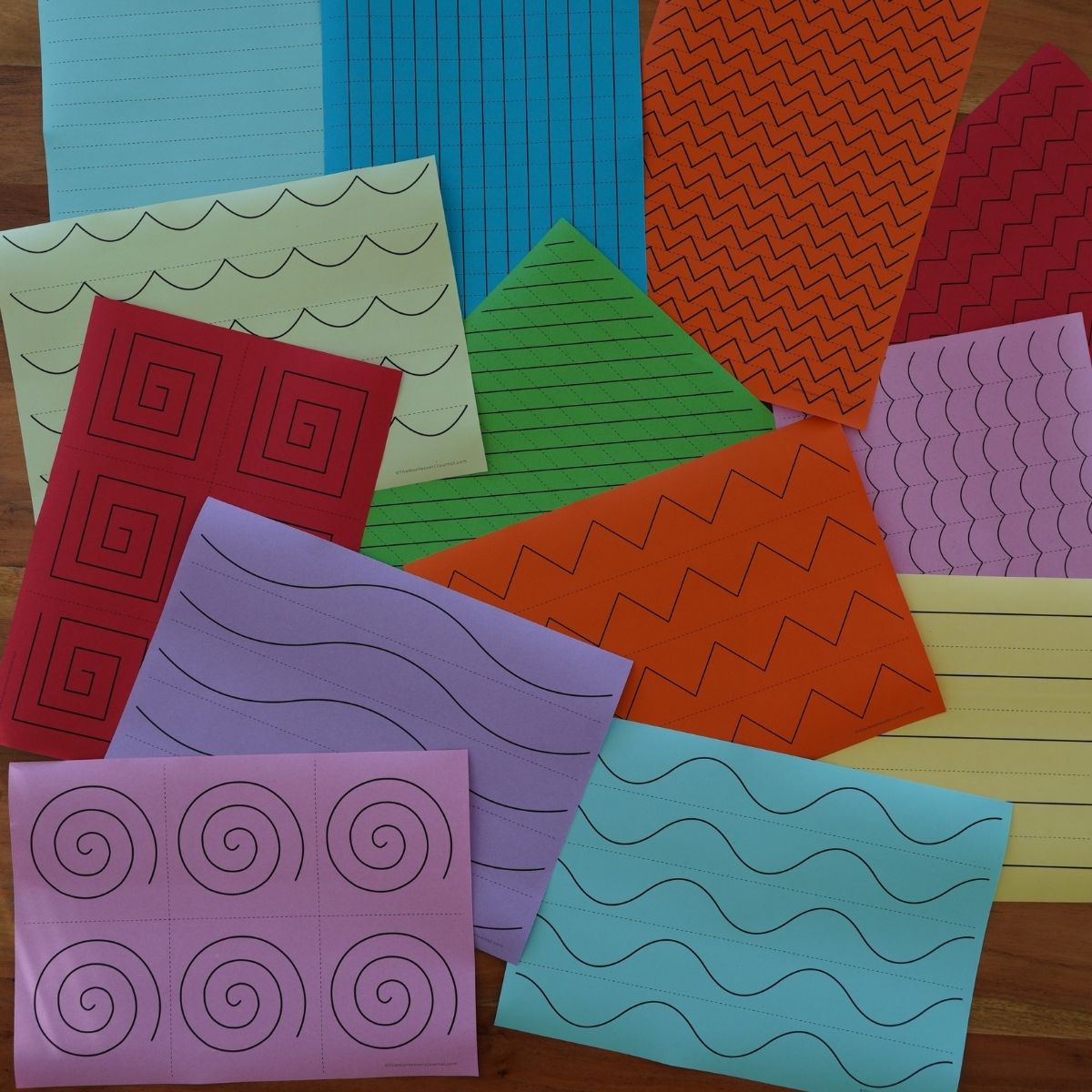 Collection of Montessori cutting strips printed on colorful paper sheets in red, orange, yellow, green, blue, and purple, each featuring different scissor practice patterns like zigzags, spirals, waves, and straight lines, arranged on a wooden surface.