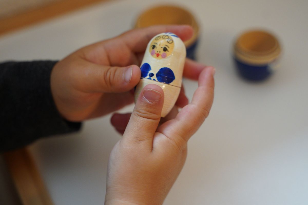 Child using Montessori hands-on learning materials, opening a wooden nesting doll to develop fine motor skills, hand coordination, and problem-solving through practical life and sensorial play
