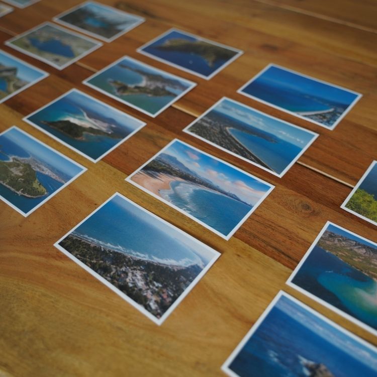 Montessori land and water form photo cards showing real images of islands, peninsulas, gulfs, and bays arranged on a wooden table for geography learning.