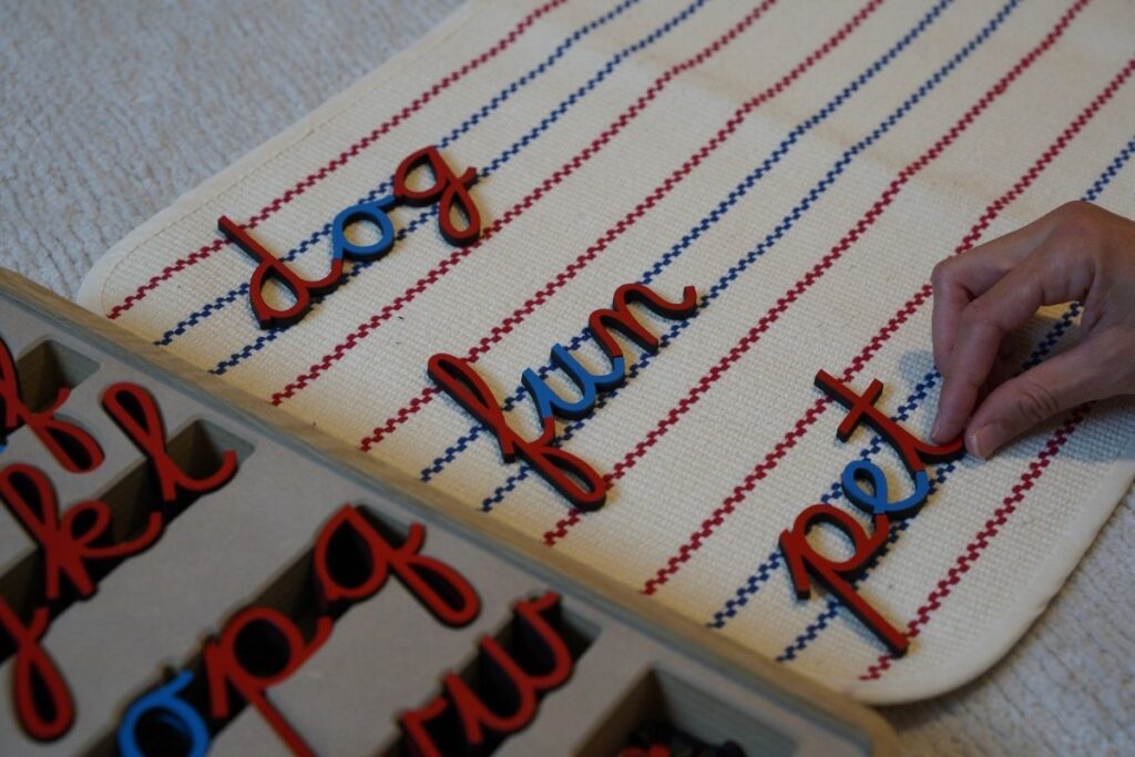 Child’s hand working with the Montessori movable alphabet, forming simple phonetic words like “dog,” “fun,” and “pet” on a textured mat to support early literacy and hands-on learning.