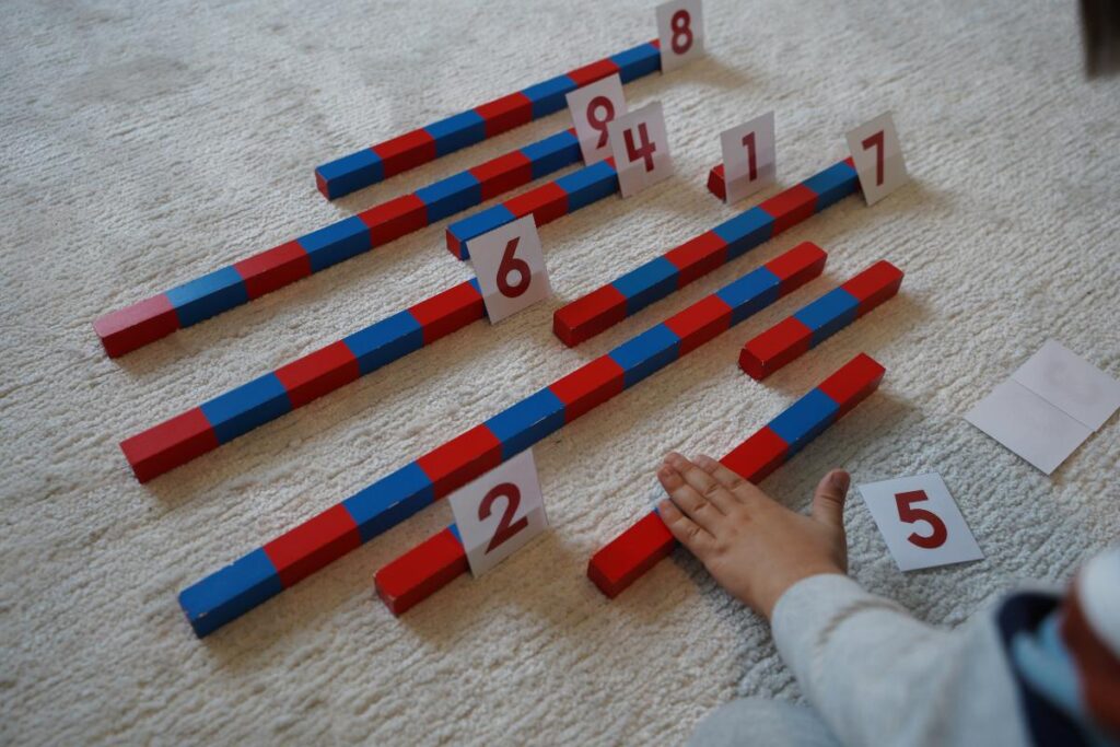 Child matching number cards to Montessori number rods on a carpet, practicing hands-on math and number recognition.