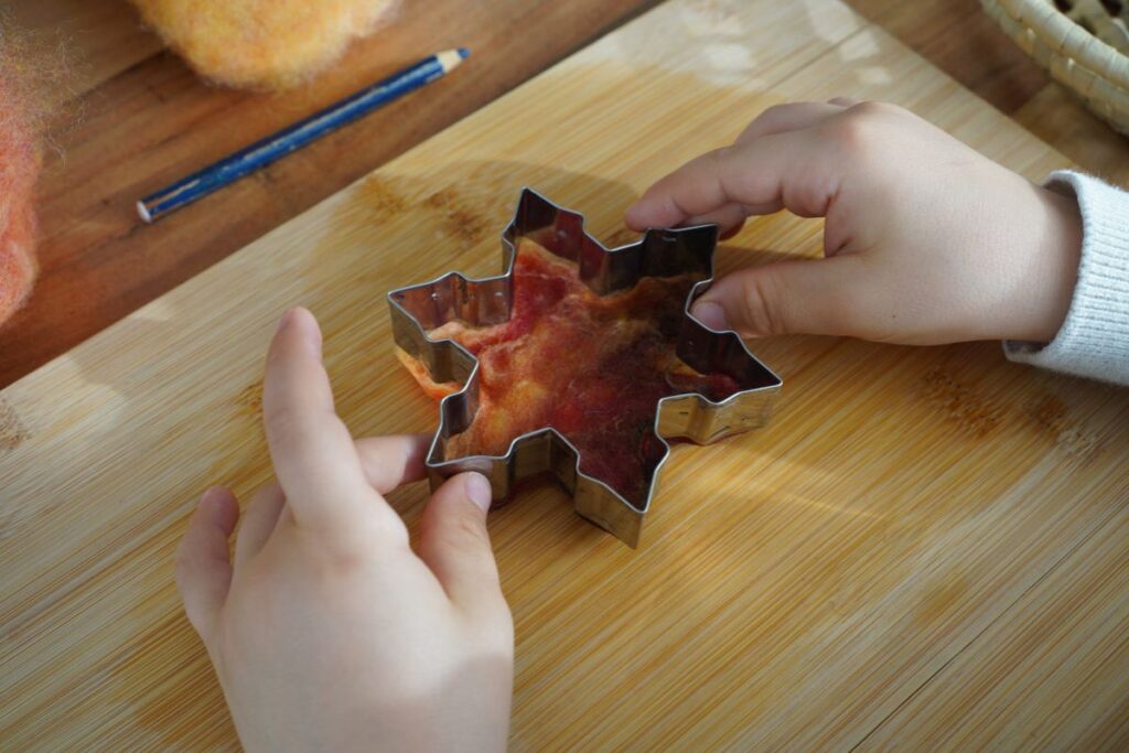 Child pressing wool roving into a star-shaped cookie cutter during a Montessori wet-felting craft to build fine motor skills.