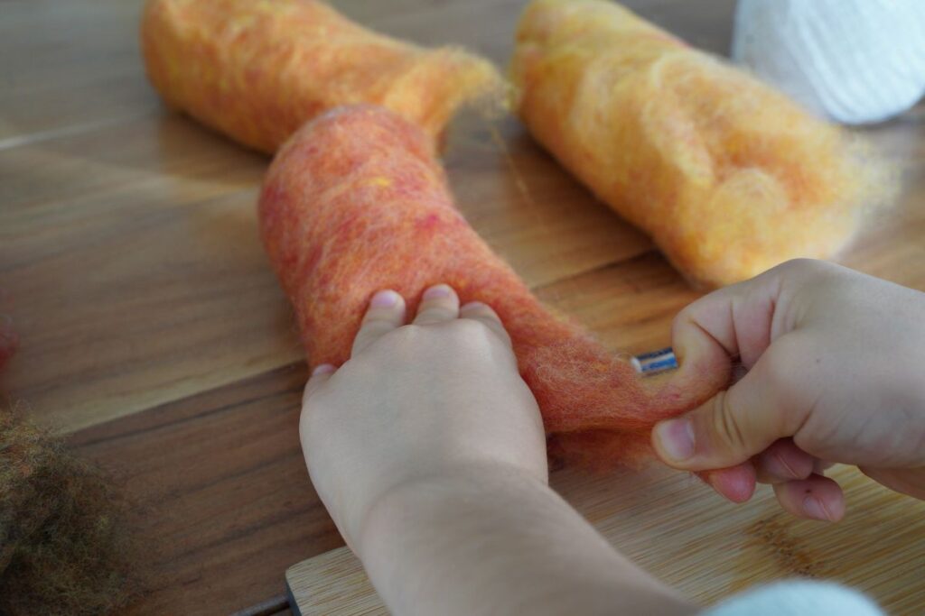 Child pulling and separating wool roving during a Montessori wet-felting activity to strengthen fine motor skills and prepare materials for a hands-on craft.