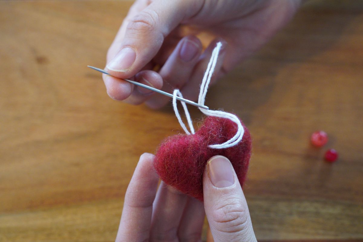 Needle and yarn being stitched through a handmade red felt heart as part of a Montessori fine motor sewing activity.