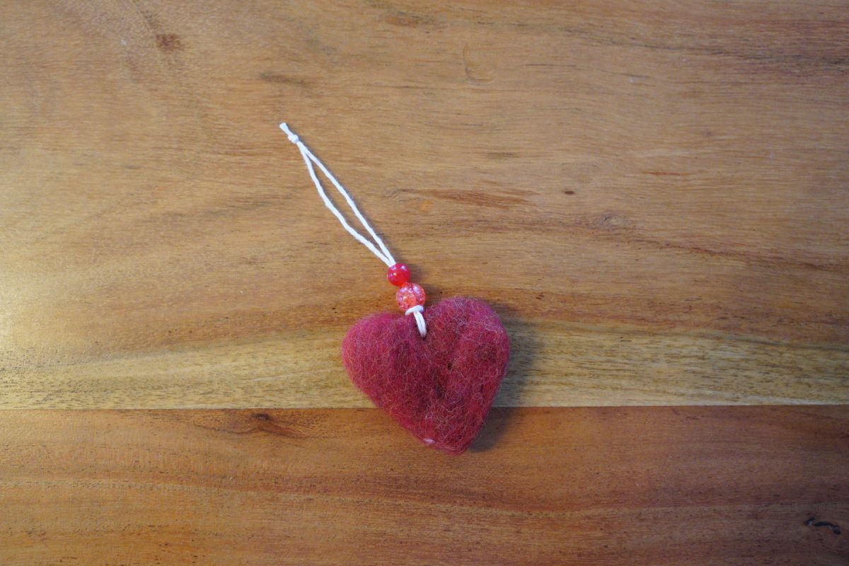 Finished red felt heart ornament with yarn loop and beads, created during a Montessori wet-felting and sewing activity.