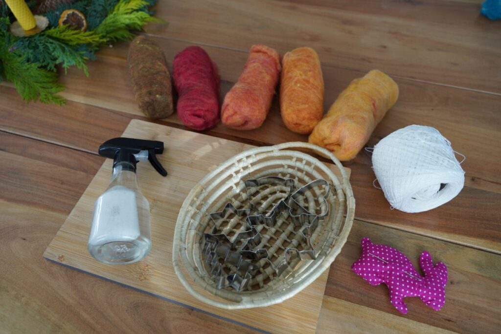 Montessori wool felting materials on a wooden table, including cookie cutters, wool roving, spray bottle, and thread for a hands-on craft activity.