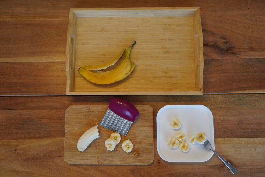 Montessori banana cutting setup with peeled banana, crinkle cutter, cutting board, and tray for practical life food prep.