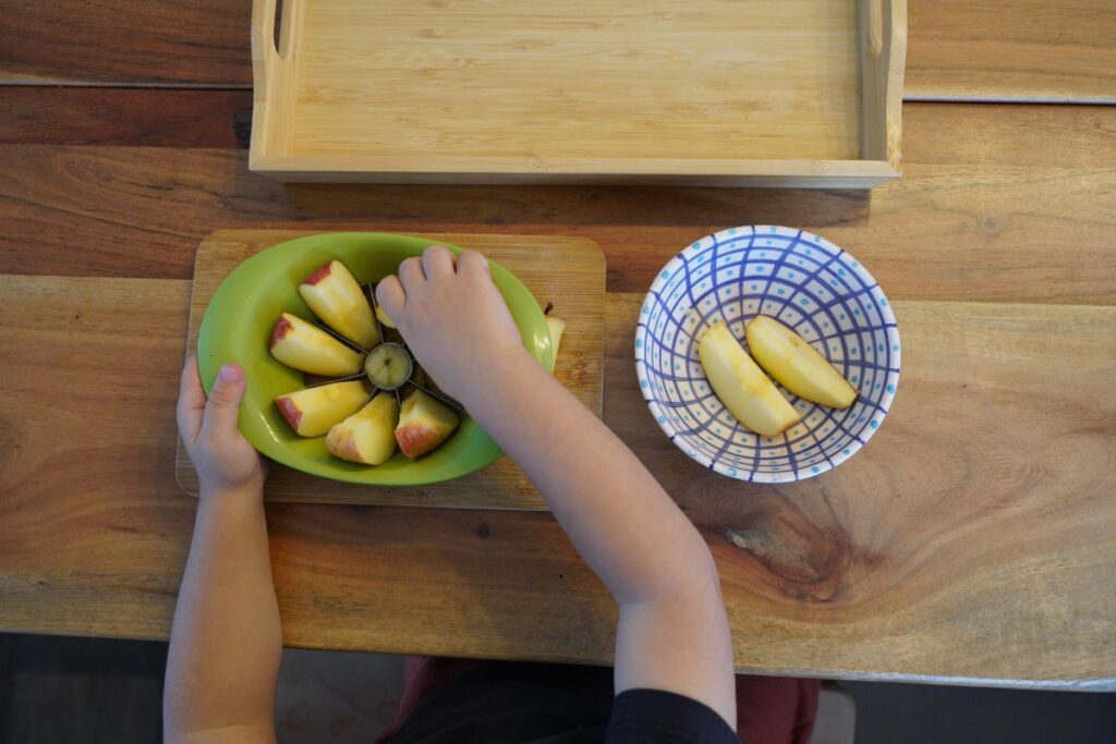 Child removing apple slices from an apple corer during a Montessori practical life fruit preparation activity.
