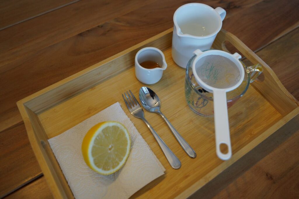 Montessori lemonade making tray with half a lemon, strainer, fork, spoons, small pitcher, and honey for practical life pouring and mixing.
