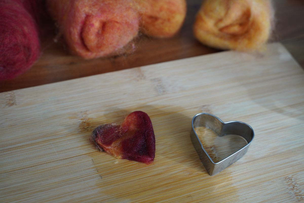 Felt heart craft removed from the cookie cutter, with wool roving materials in the background during a Montessori hands-on activity.