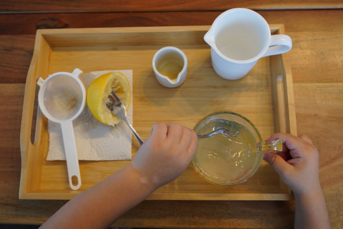 Child mixing freshly squeezed lemon juice with water and honey during a Montessori practical life lemonade activity.