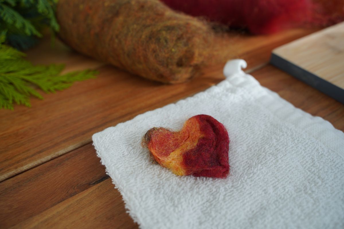 Finished wet-felted heart drying on a white towel as part of a Montessori wool felting activity for children.
