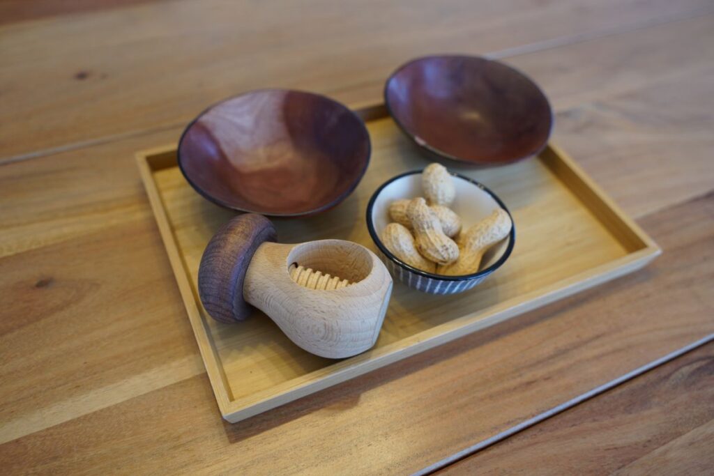 Montessori practical life tray with peanuts, bowls, and a wooden nutcracker for a hands-on food preparation activity.