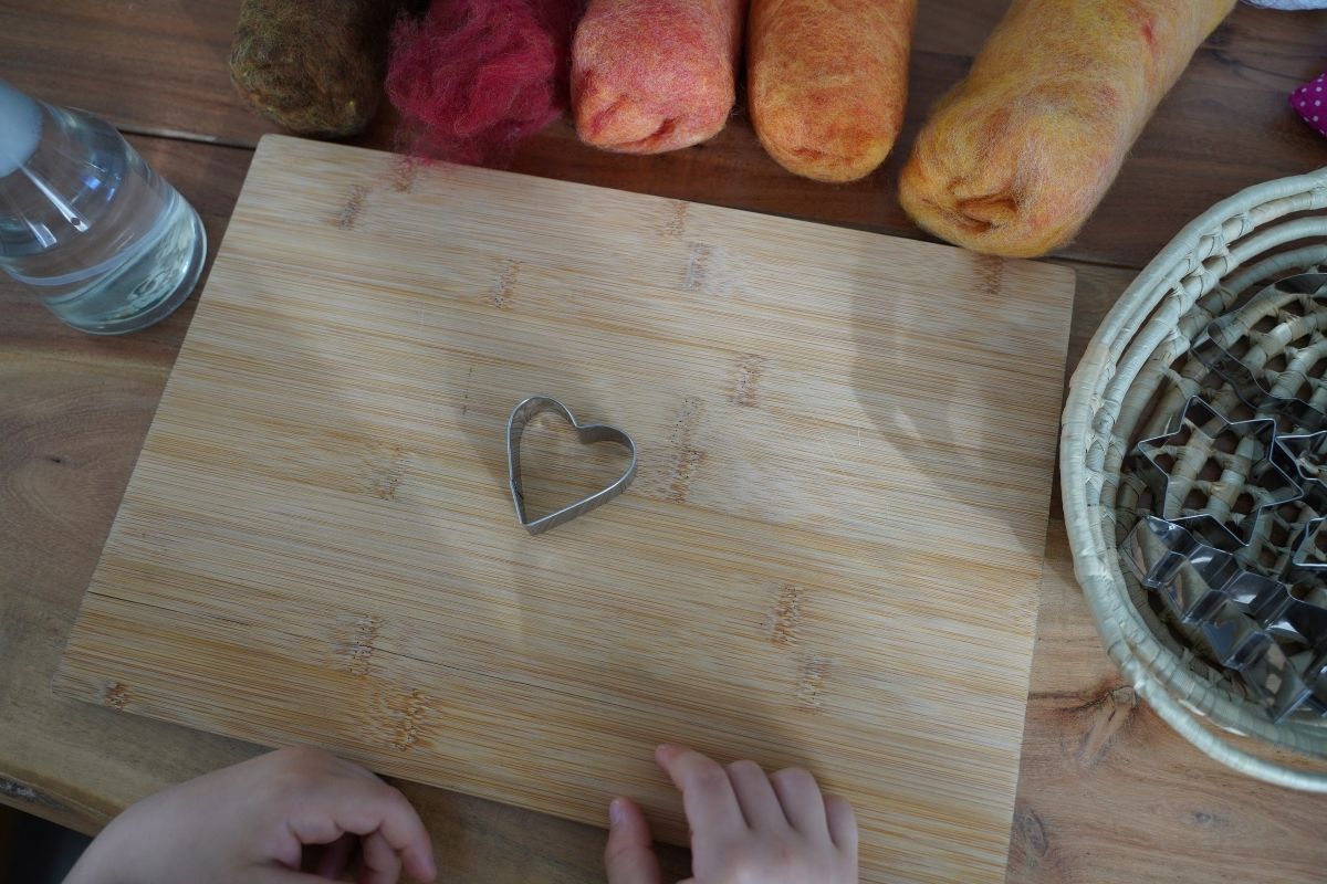 Montessori felt crafting setup with wool roving, cookie cutters, spray bottle, and a child preparing a heart-shaped wet felting activity.